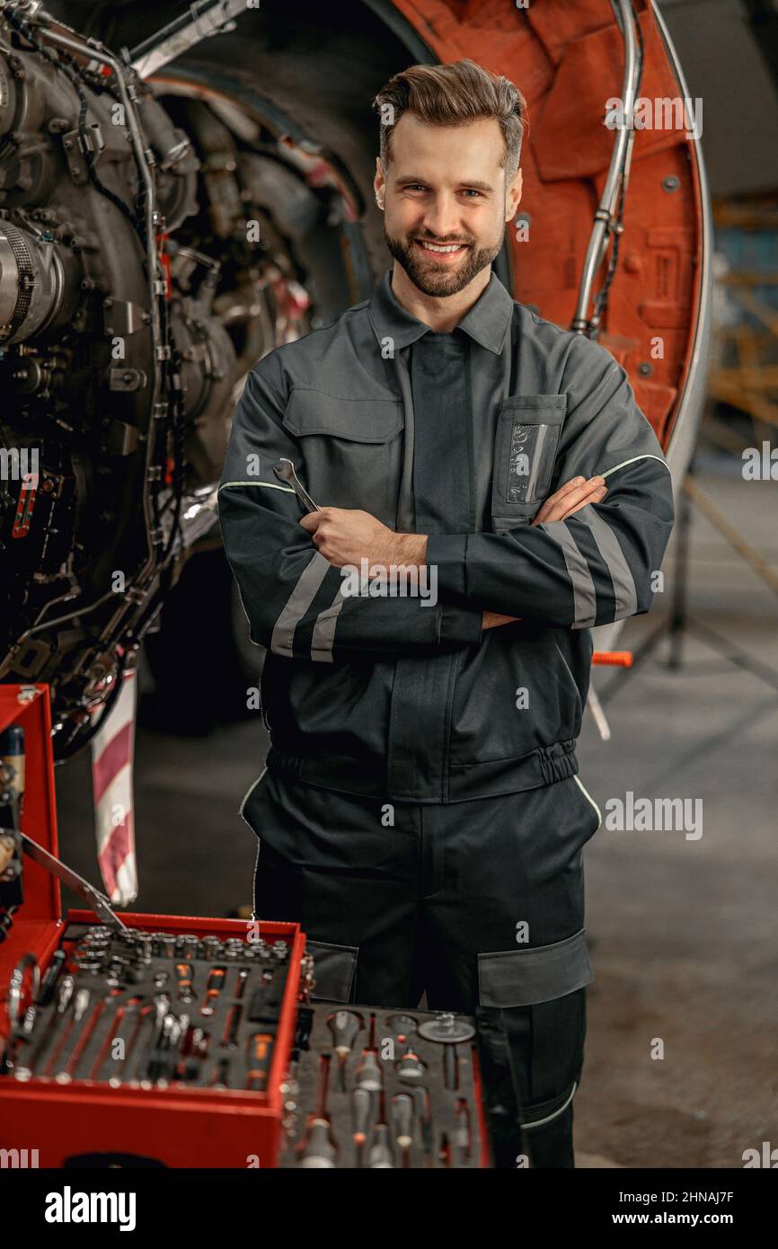 Fröhlicher Flugzeugmechaniker, der in der Nähe des Werkzeugkastens im Hangar steht Stockfoto