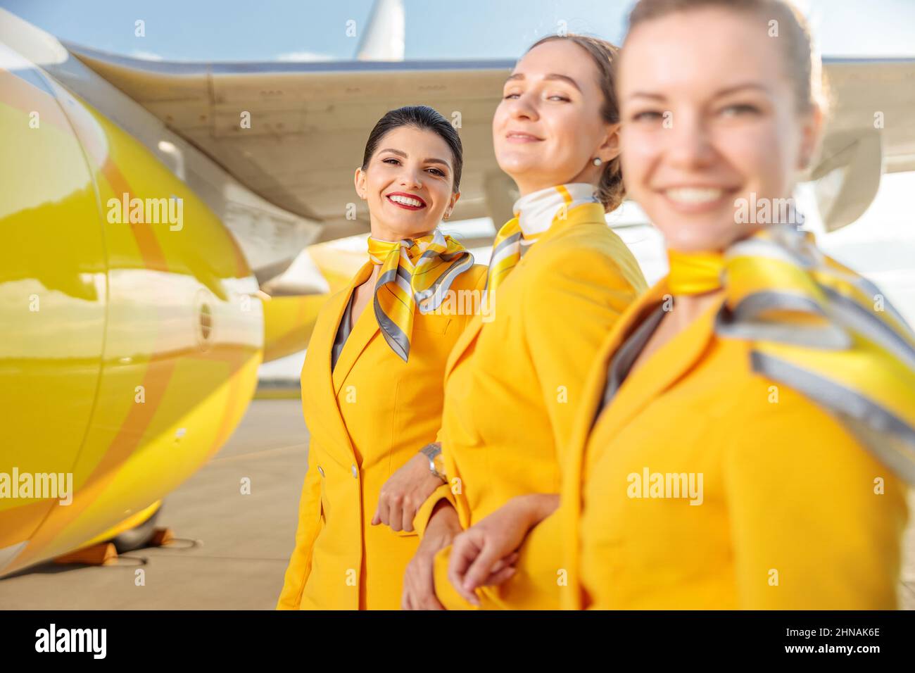 Fröhliche weibliche Flugbegleiterinnen, die in der Nähe von Flugzeugen am Flughafen stehen Stockfoto