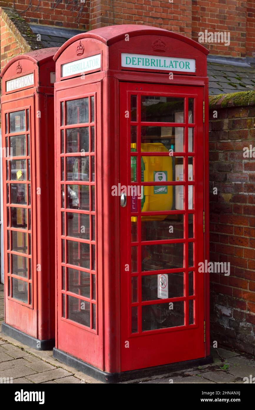 Rote traditionelle Telefonbox, die für den öffentlichen Defibrillator neben der eigentlichen Telefonbox in Hampshire, Großbritannien, verwendet wurde Stockfoto