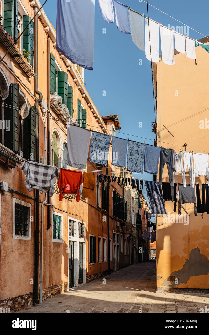 Wäsche hängt aus der typischen venezianischen Fassade, Italien. Enge Straße mit bunten Gebäuden und Kleidung trocken am Seil, Venedig. Saubere Kleidung trocknen im Freien Stockfoto