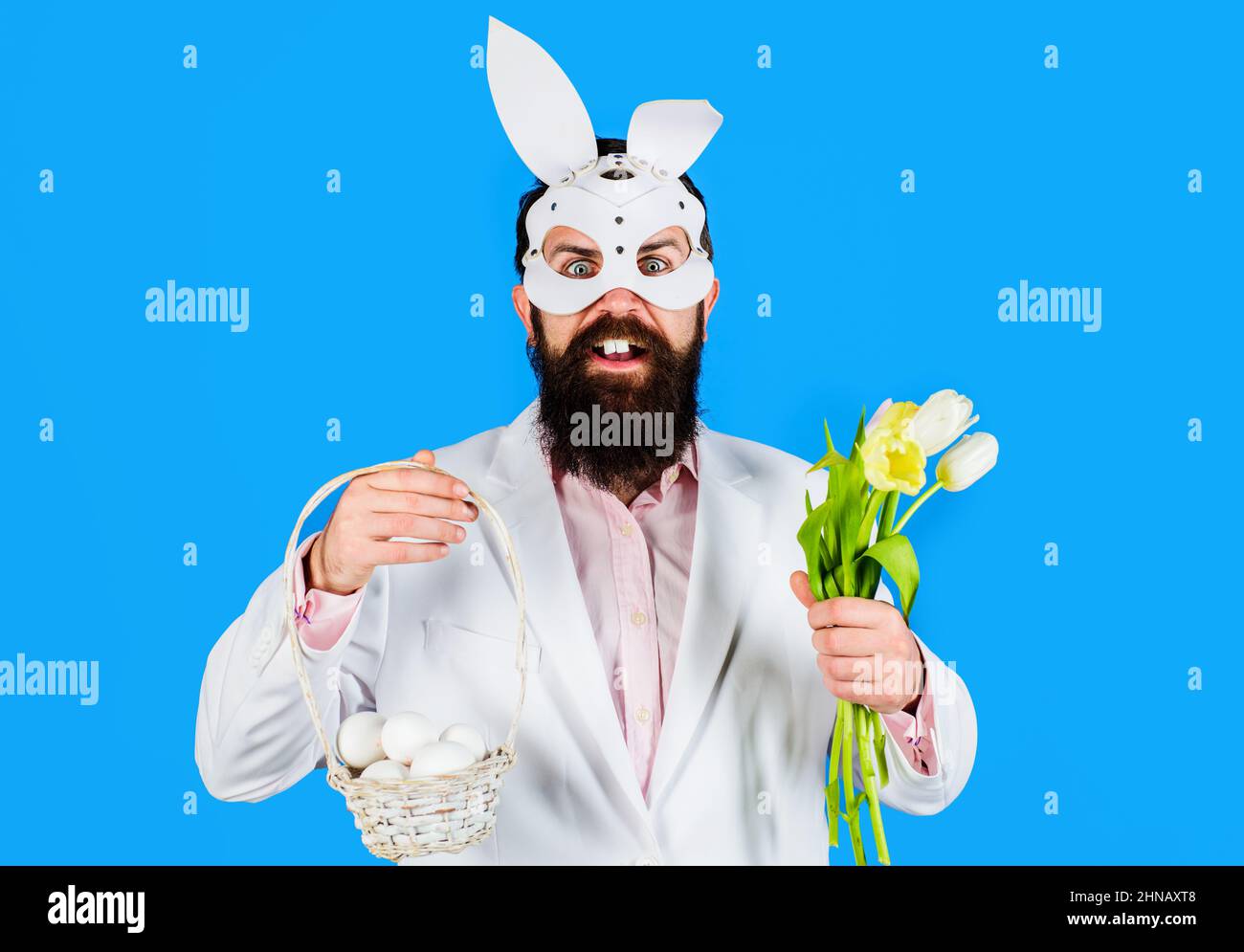 Bärtiger Mann in Hasenohren mit Korbeiern und Tulpenstrauß. Rabbit man. Ostertag. Frühlingsangebot. Rabatt. Stockfoto