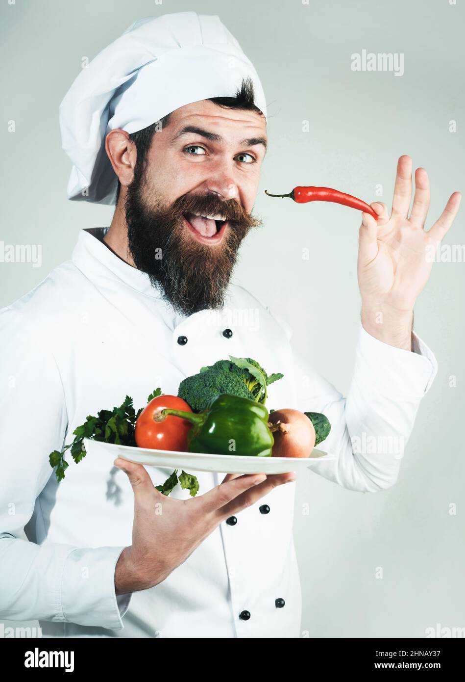 Koch in Uniform mit Chilli und Teller mit Gemüse in den Händen. Grünes Lebensmittelgeschäft. Bio-Lebensmittel Stockfoto