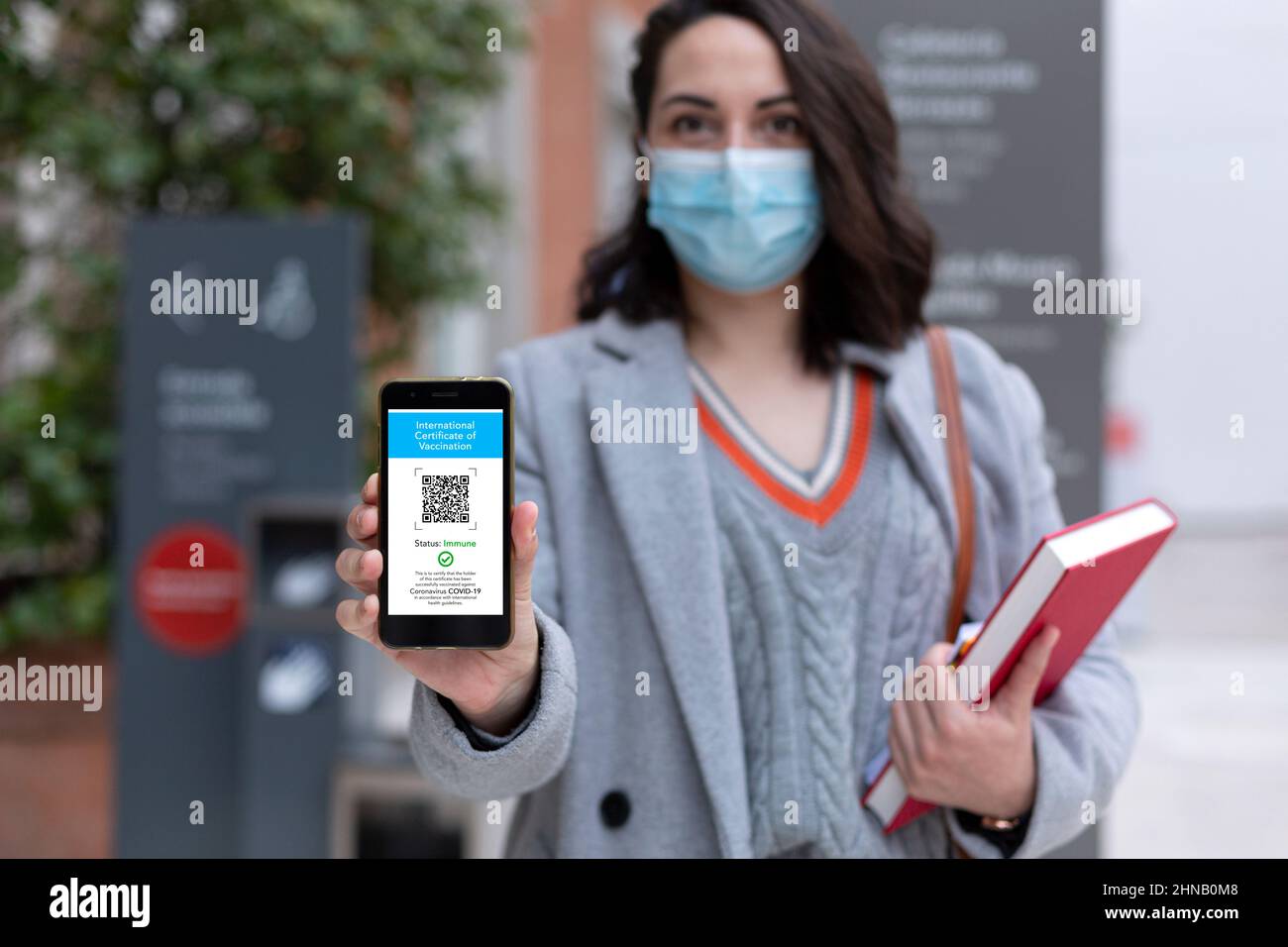 Studentin mit Gesichtsmaske, die Smartphone mit digitalem Impfpass auf dem Bildschirm hält. Selektiver Fokus. Stockfoto