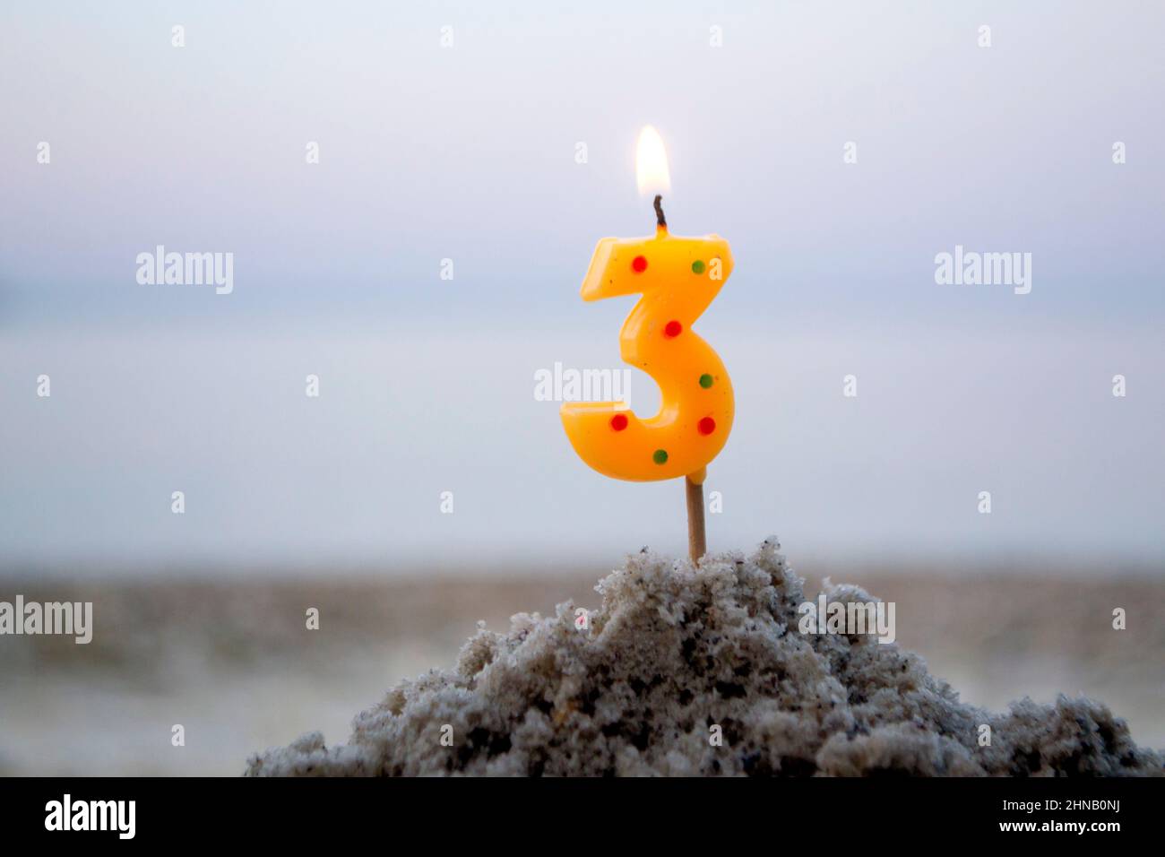 Kerze Nummer drei auf Stock in Sand gesteckt und verbrennt. Brennende Kerze Stockfoto