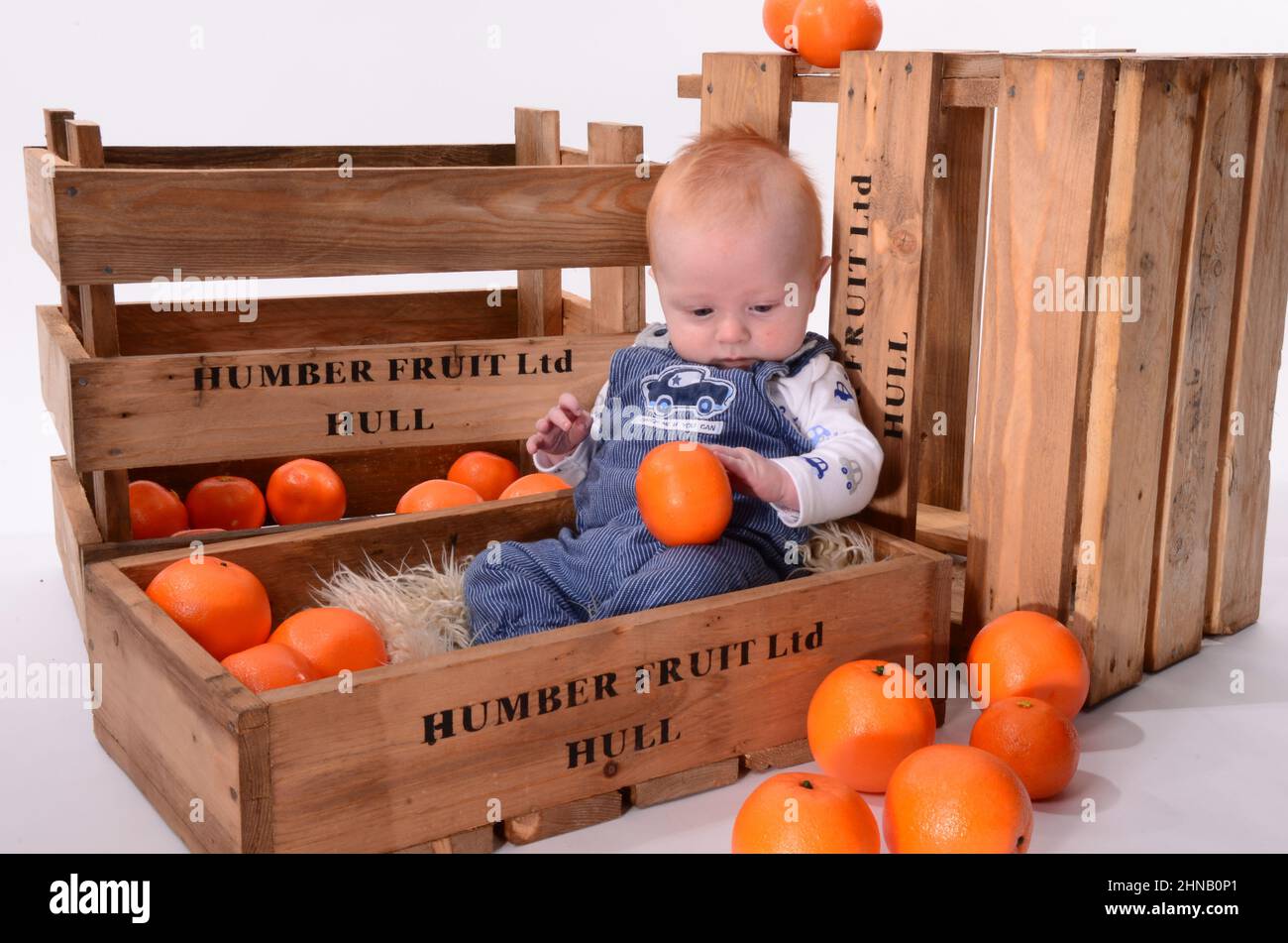 Fröhlicher kleiner Junge mit roten Haaren, der in einer orangen Obstkiste spielt Stockfoto