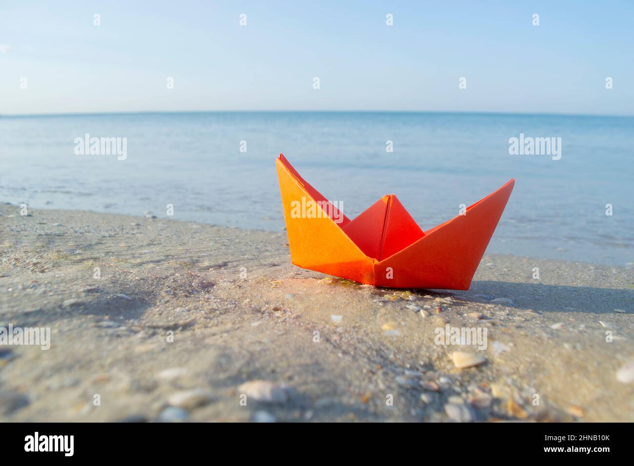 Kleines orangefarbenes Boot auf Sand in der Nähe des Wassers vor dem Hintergrund der Meereswellen Stockfoto