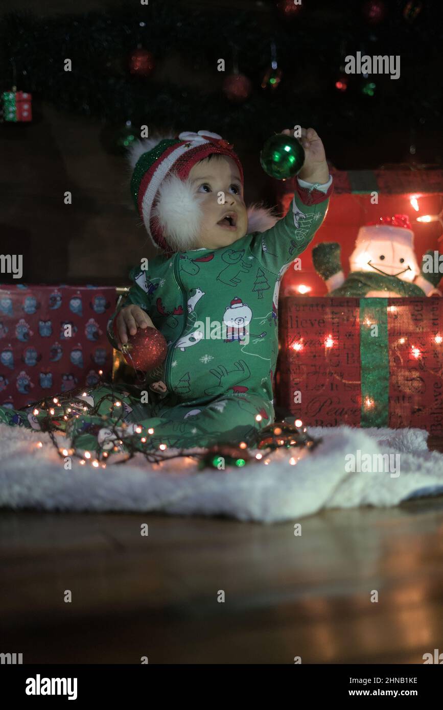 Eine vertikale Aufnahme eines kaukasischen Kindes in einem grünen Weihnachtskostüm, das mit Weihnachtsspielzeug spielt Stockfoto