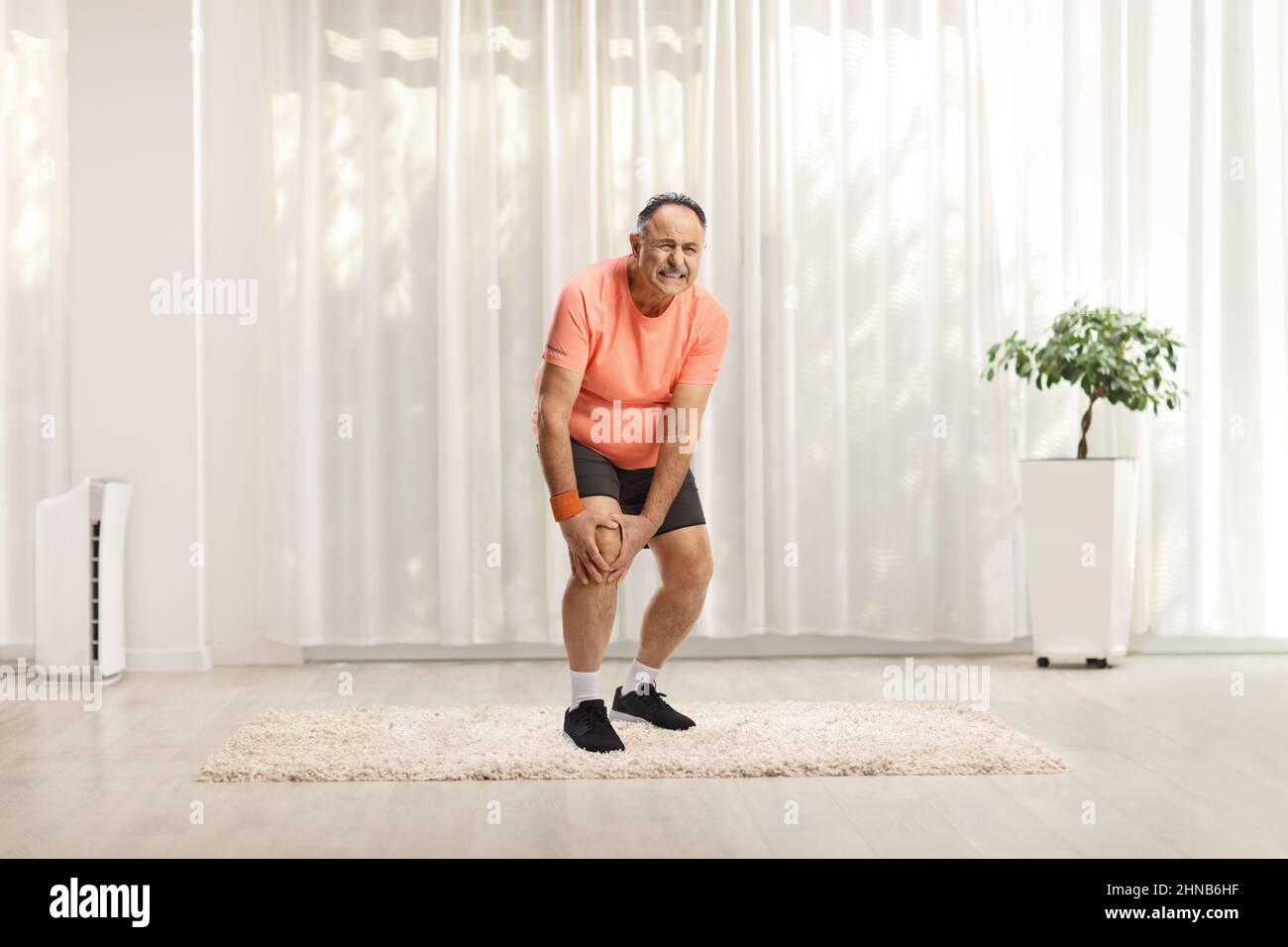 Reifer Mann in Sportkleidung, der sein schmerzhaftes Knie in einem Raum hält Stockfoto