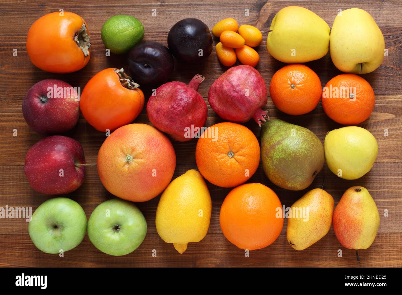 Verschiedene Obstsorten auf einem braunen Holztisch. Blick von oben. Nahaufnahme. Kaki, Äpfel, Pflaumen, Granatäpfel, Birnen, Orangen, Mandarinen Stockfoto