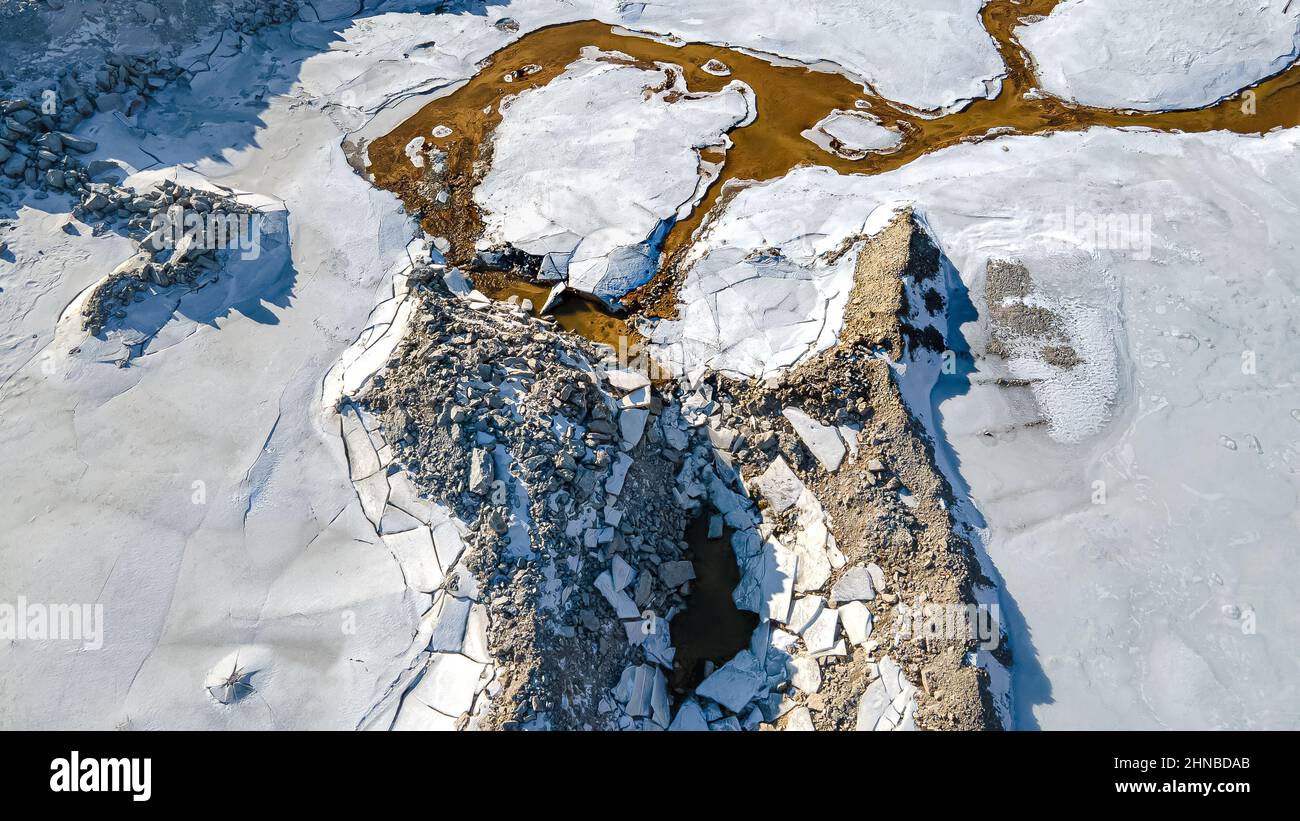 Das Eis ist gebrochen, als Schnee am Steinbruch schmilzt und einen kleinen Bach im Schmutz bildet. Stockfoto