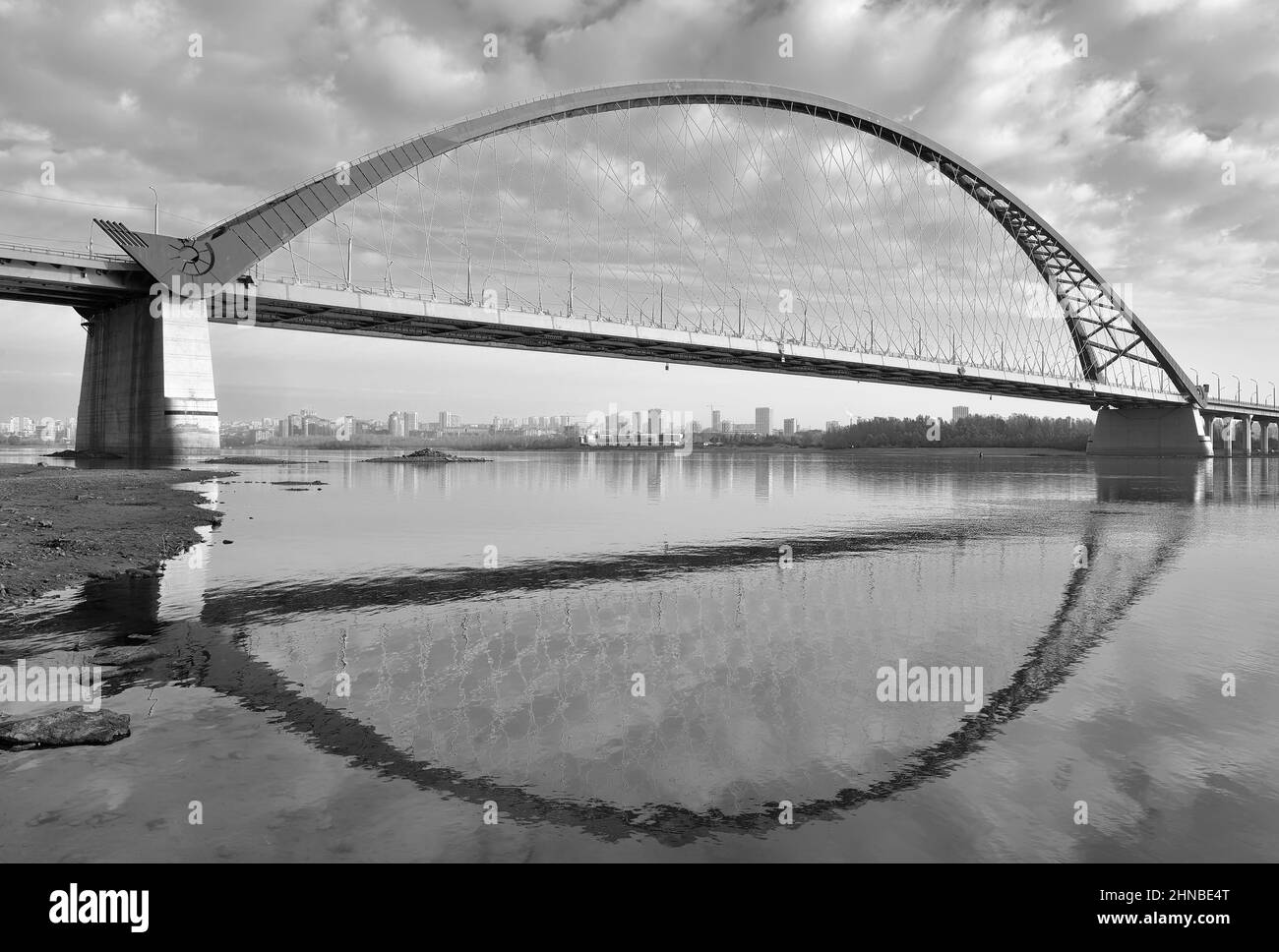 Das Ufer des ob. Bugrinski Bogenbrücke mit Spiegelung im Wasser am Rande der großen Stadt. Nowosibirsk, Sibirien, Russland, 2021 Stockfoto