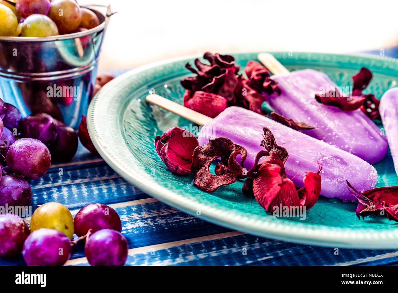 Ein Traubeneis im Lollipop-Stil auf einem Stock auf einem Vintage-Teller auf einem hellblauen Holztisch. Konzept der natürlichen und gesunden Ernährung. Stockfoto