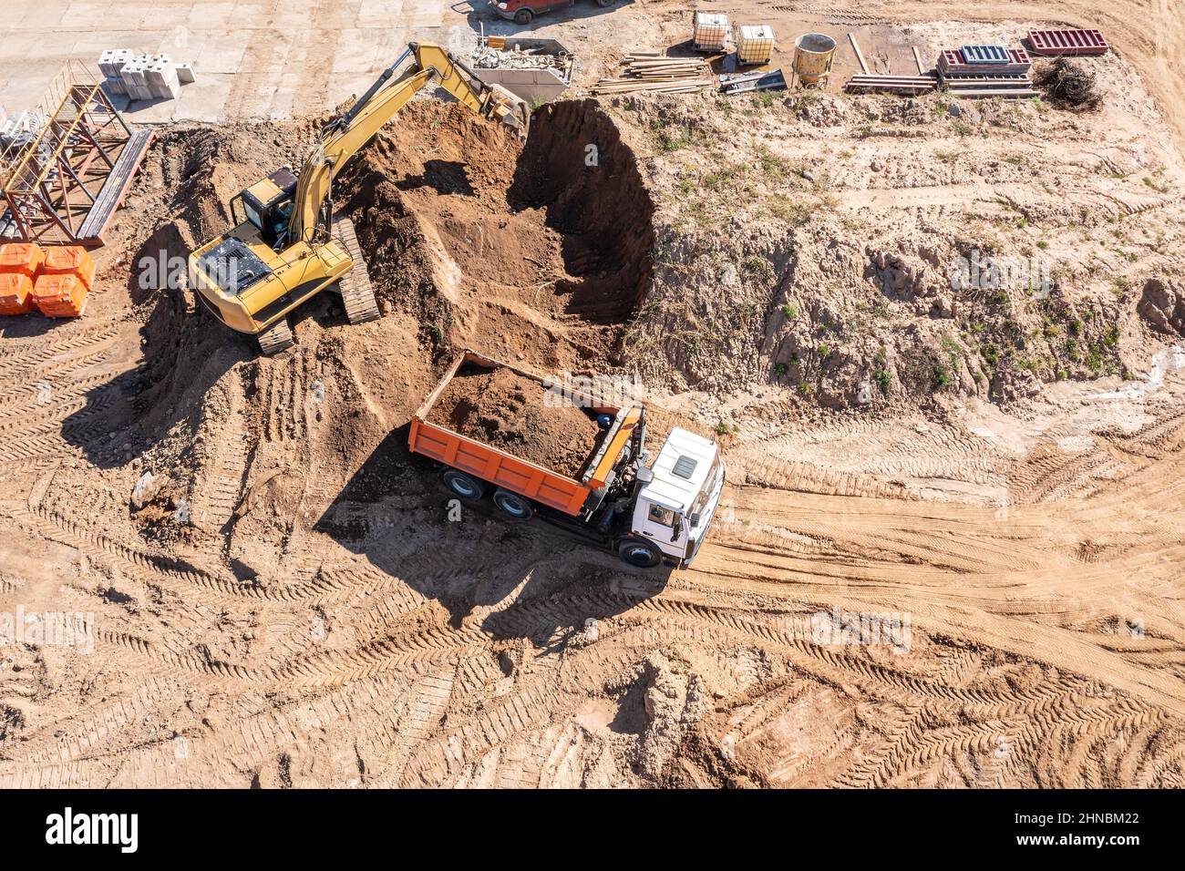 Bagger lädt Sand in einen LKW auf der Baustelle. Luftaufnahme von oben von einer Drohne. Stockfoto