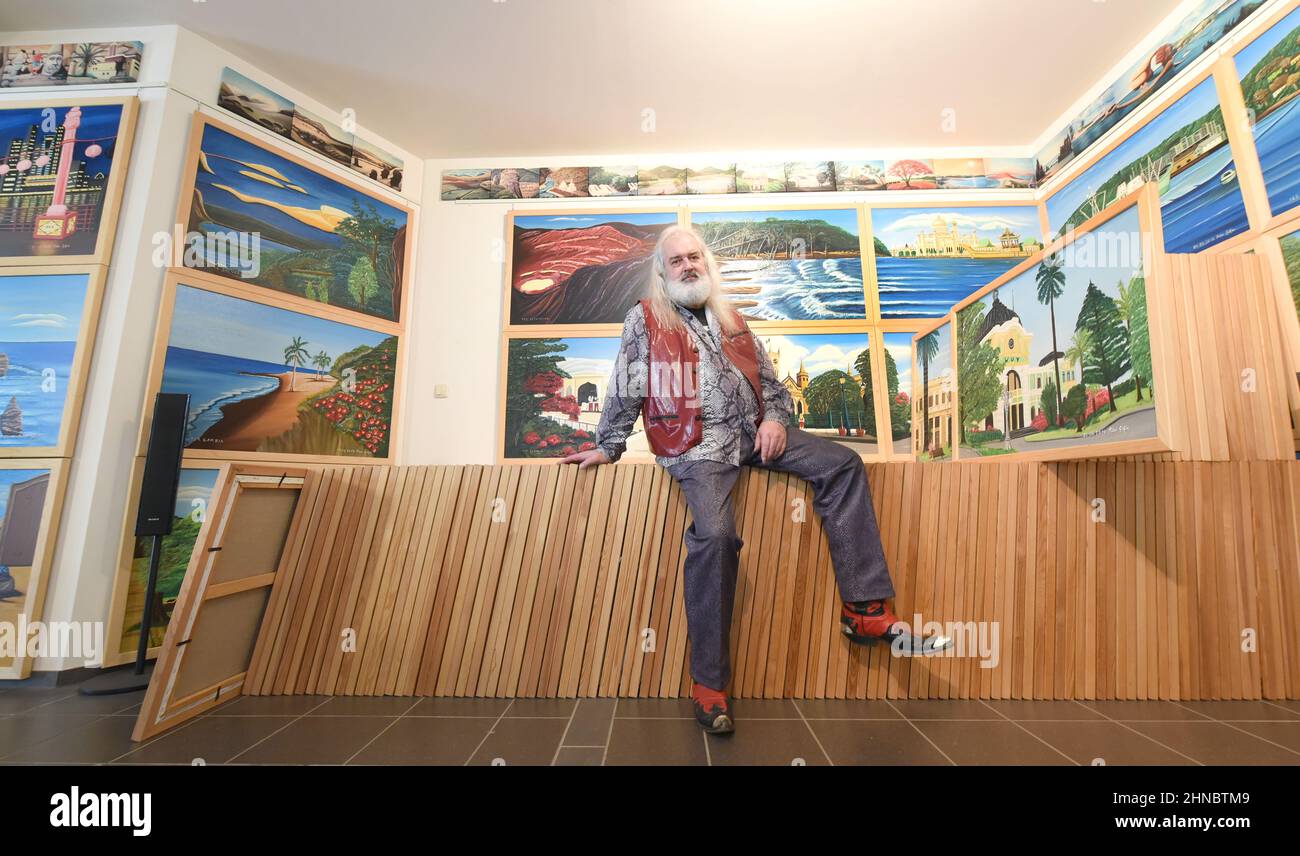 14. Februar 2022, Sachsen-Anhalt, Spergau, bei Leuna: Der Künstler Peter Gehre sitzt in seinem Wohnzimmer, das er auch als Atelier, Musikraum und Büro nutzt, auf gestapelten Bildern seines 192 Meter langen Gemäldes, dem längsten der Welt. Der 65-Jährige sucht dringend nach einem Ausstellungsort, oder, wie er sagt, einem Millionär, für seine „The World Union Vision“, die aus 192 Ölgemälden besteht. Die Verbindung und der nahtlose Übergang von einem Gemälde und damit von einem Land zum anderen ist die Vision des 65-Jährigen von Gleichberechtigung für alle Länder und einer friedlich vereinten Welt. (To dpa 'Pai Stockfoto