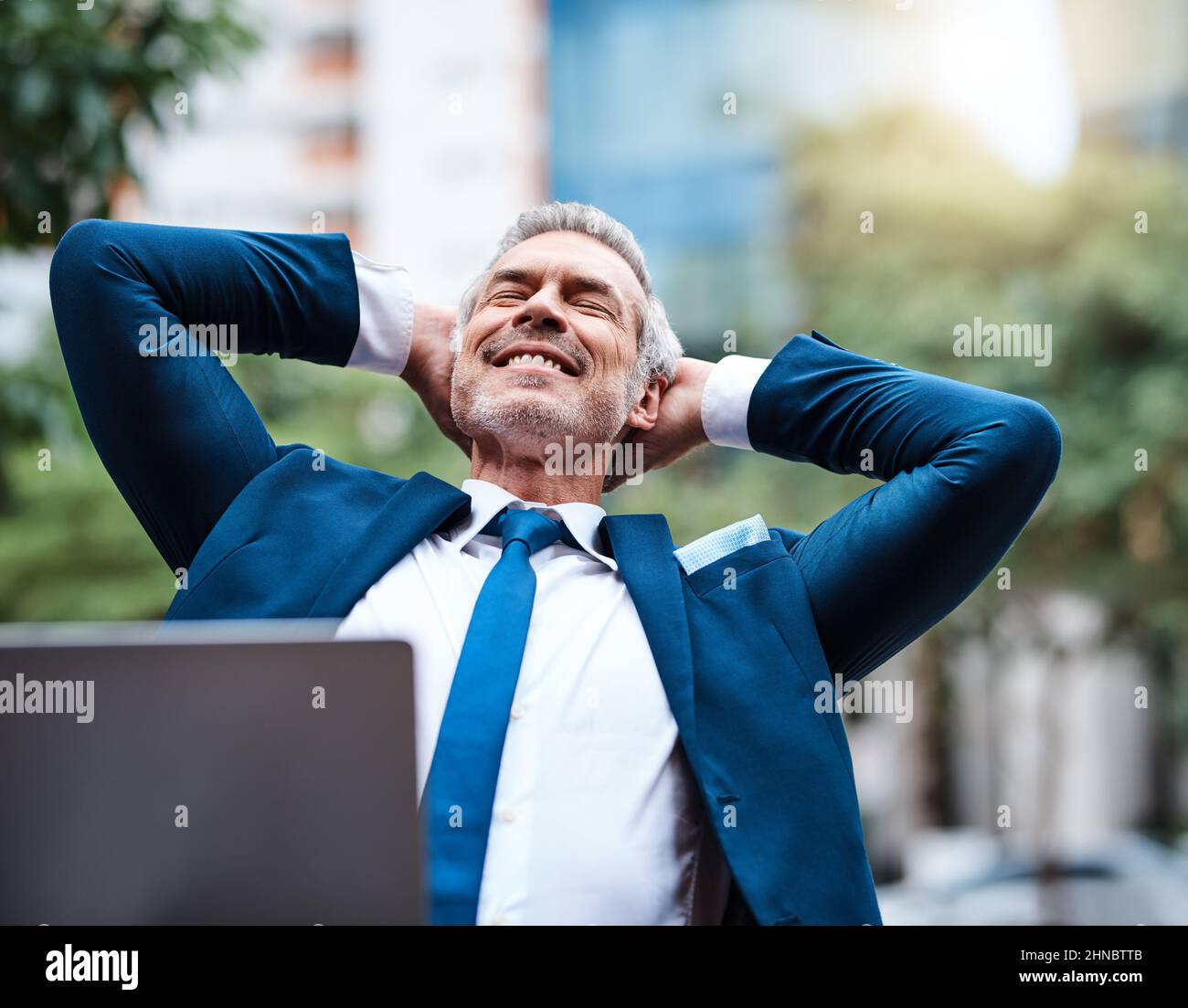 Nehmen Sie sich etwas Zeit vom Büro. Aufnahme eines fröhlichen, reifen Geschäftsmannes mit den Händen hinter dem Kopf, der tagsüber draußen entspannt. Stockfoto