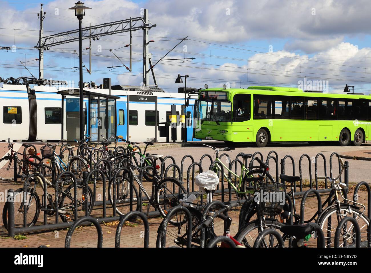 Gnesta, Schweden - 3. September 2021: Fahrräder vor einem grünen öffentlichen Transportbus am Bahnhof mit einem SL-Pendlerzug. Stockfoto