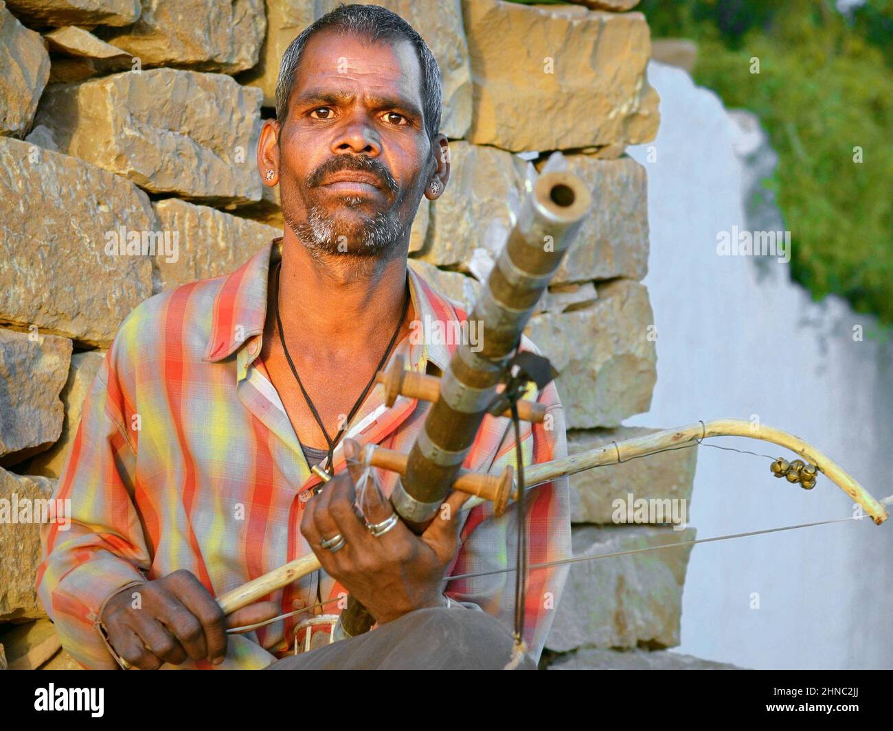 Der indische Straßenmusiker spielt bei Sonnenuntergang seine traditionelle Ravanahatha (altes indisches Saiteninstrument) und schaut auf den Zuschauer. Stockfoto