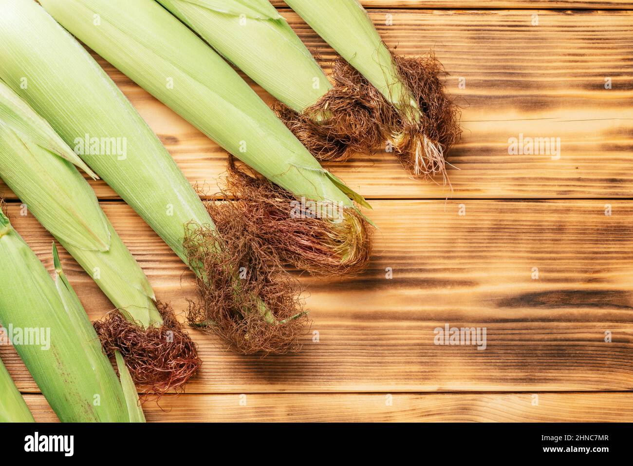 Süße frische grüne Milch Maiskolben-Ohrblätter liegen auf braun gebranntem Holztisch Hintergrund. Maisbraun lockiges Haar. Flach liegend, Draufsicht. Speicherplatz kopieren Stockfoto