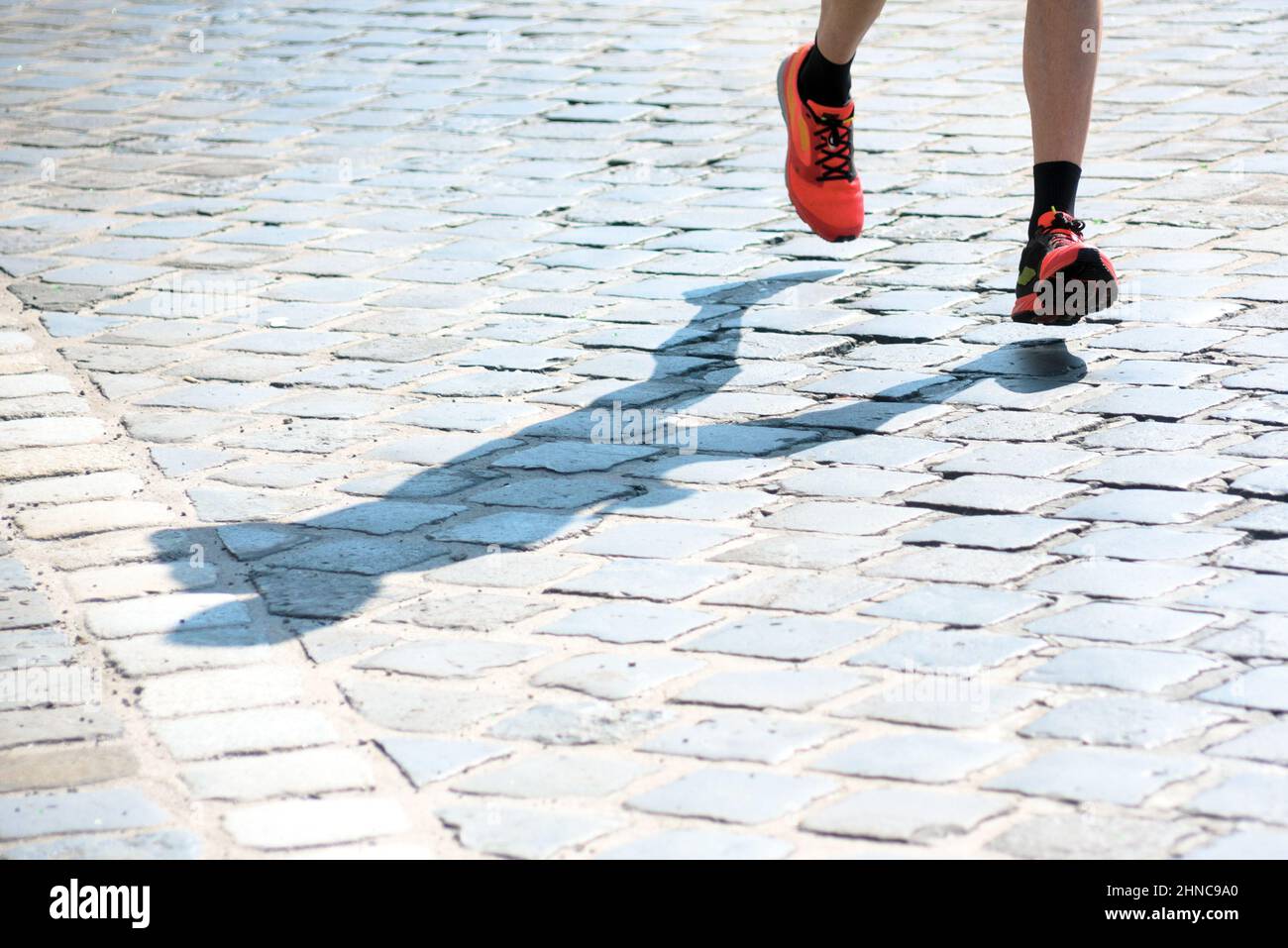 Füße und Schatten einer Person, die auf dem Bürgersteig läuft Stockfoto