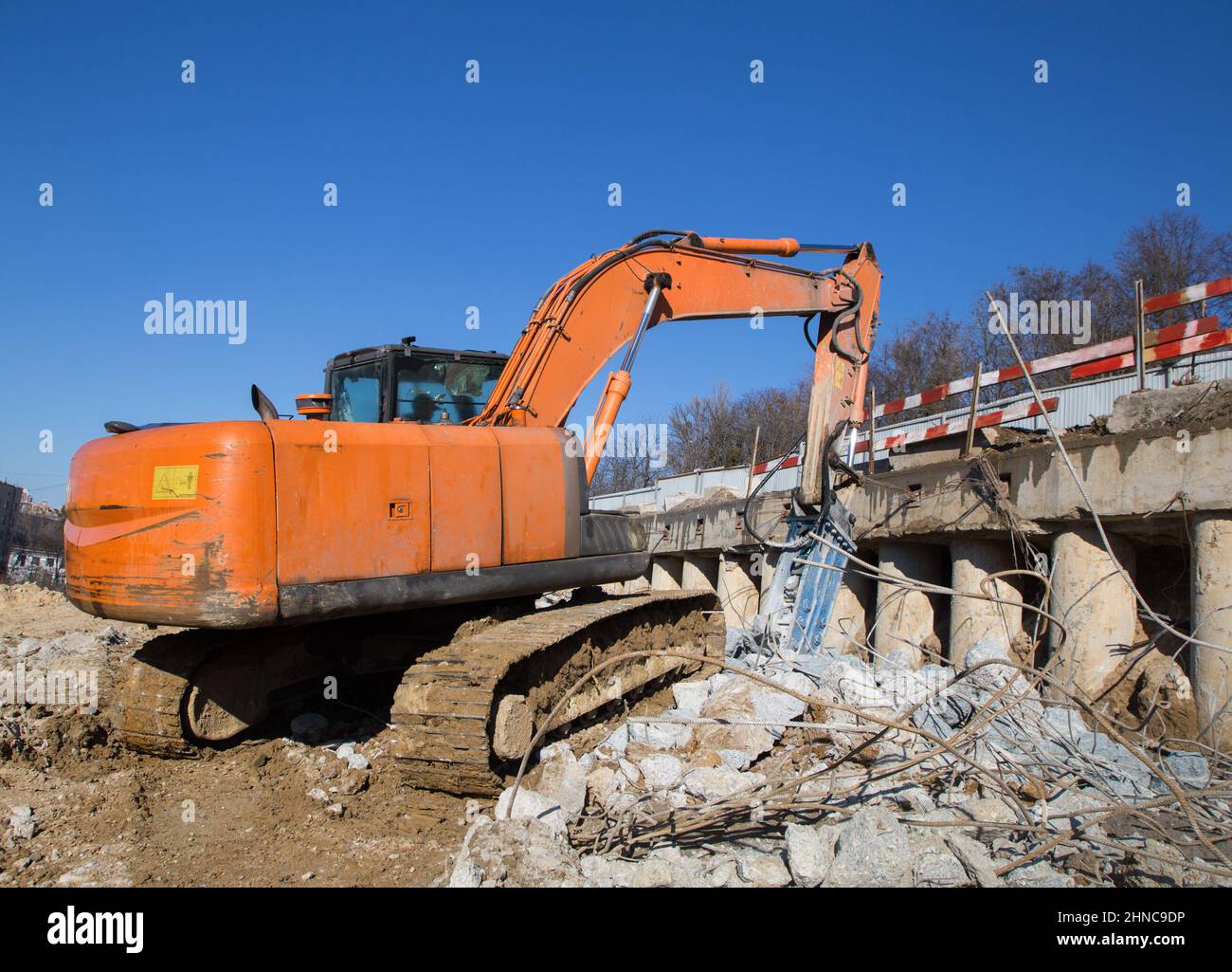 Auf einer Baustelle arbeitet ein orangefarbener Bagger mit industriellem Hydraulikhammer. Teile aus Beton und Metallbeschlägen. Stockfoto