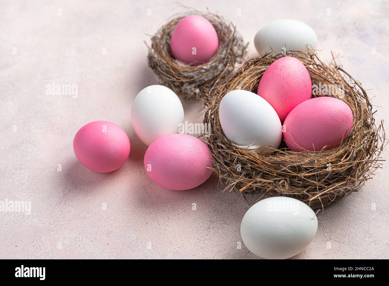 Frohe Ostern, ein Nest mit weißen und rosa Ostereiern auf einem zarten pastellfarbenen Hintergrund. Seitenansicht. Stockfoto