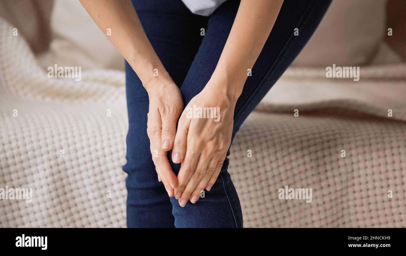 Beschnittene Ansicht einer Frau, die schmerzhaftes Knie berührt, während sie zu Hause steht Stockfoto
