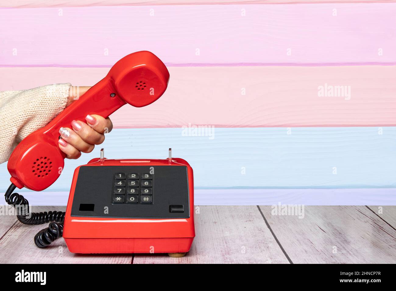 Eine feminine elegante, wunderschön gepflegte Frauenhand, die einen alten roten Telefonhörer über eine abstrakt gestreifte Hintergrundstruktur hält. Kommunikation BAC Stockfoto