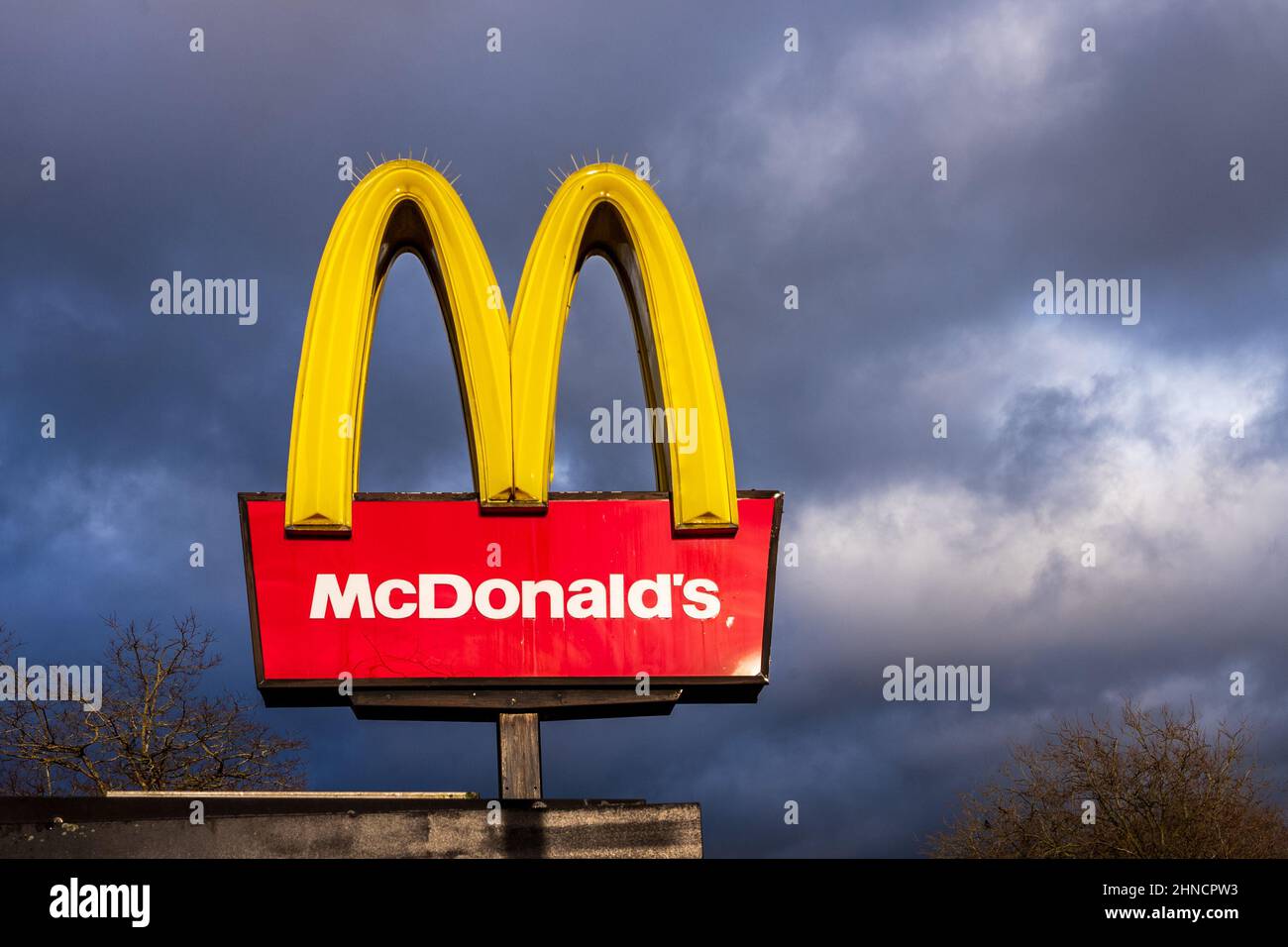 McDonalds Zeichen gegen einen stürmischen Himmel. McDonalds UK Restaurant Schild sonnenbeleuchtet vor dunklen Sturmwolken. McDonalds Fast Food Restaurant Milton Keynes, Großbritannien. Stockfoto
