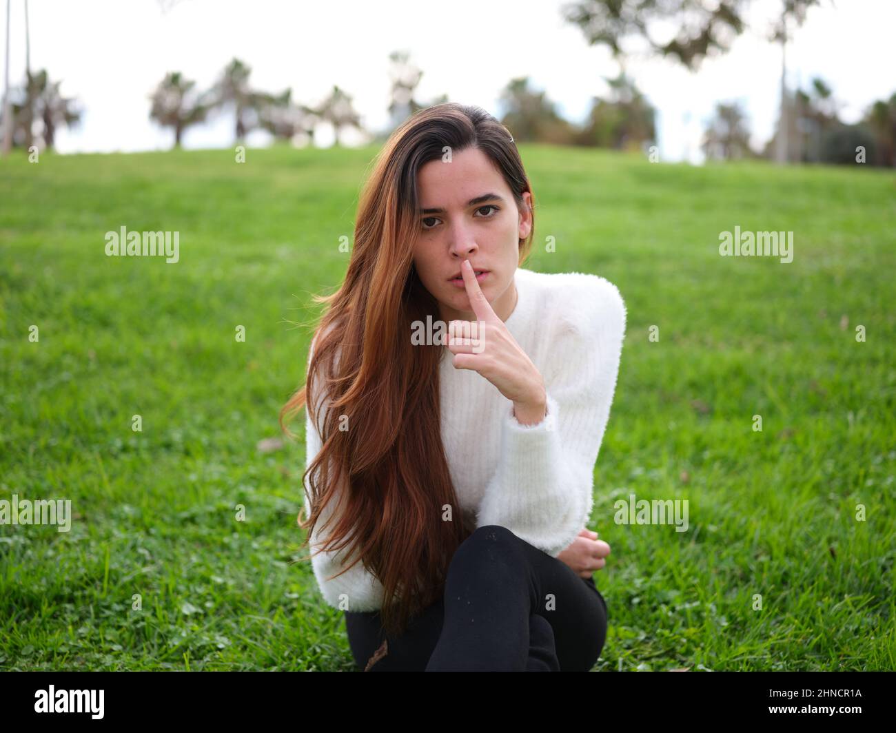 Eine junge Frau im Park, die auf dem Gras sitzt und um Ruhe bittet. Stockfoto