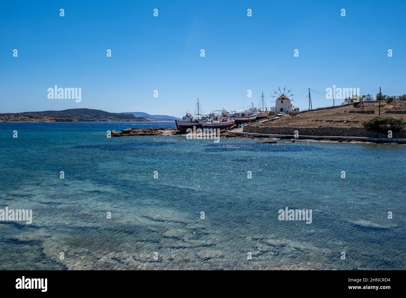 Griechenland. Ano Koufonisi Insel, Kykladen. Traditionelle Windmühle über alte Schiffswerft für hölzerne Fischerboote reparieren. Ägäis funkelt Meer, sonniger Tag, Stockfoto