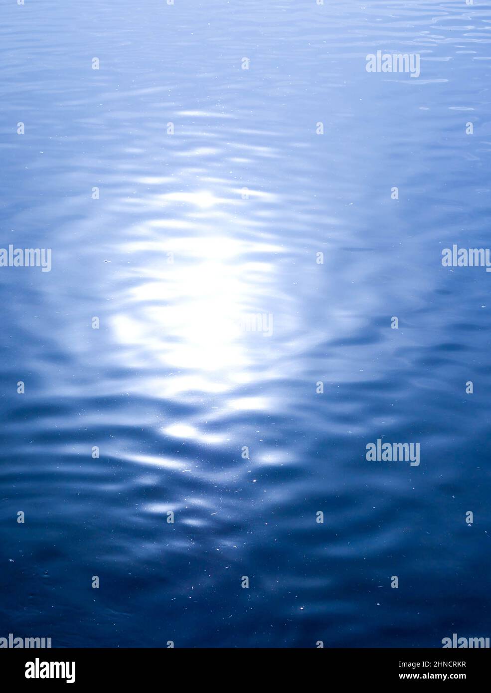 Heller Sonnenfleck, der sich vom ruhigen blauen Wasser abspiegelt Stockfoto