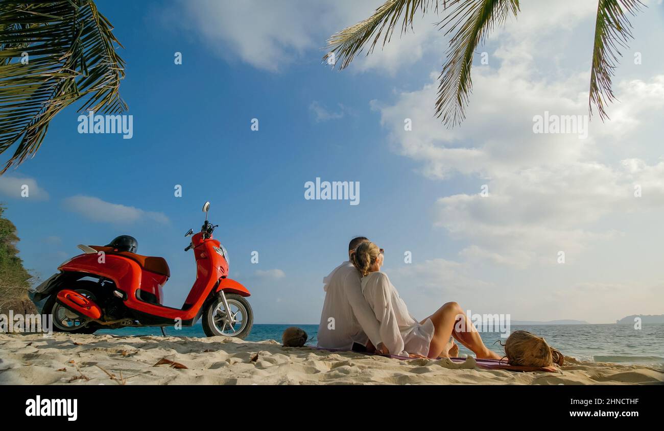 Motorroller Road Trip. Schönes Paar auf rotem Motorrad in weißen Kleidern am Sandstrand. Hochzeit gerade verheiratete Menschen, die in der Nähe von tropischen Palmen, Meer. Flitterwochen am Meer. Asien Thailand. Motorradmiete. Stockfoto