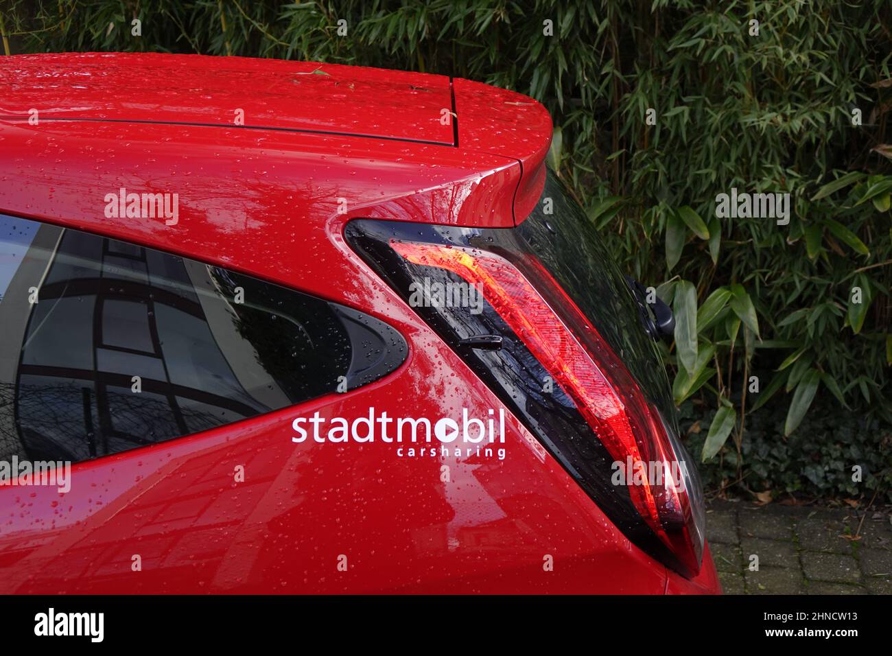 9. Januar 2022, Kaiserslautern, Deutschland, Rückenteil eines roten Stadtmobil-Carsharing-Autos mit grünen Büschen im Hintergrund, grüne Mobilität (horizontal) Stockfoto