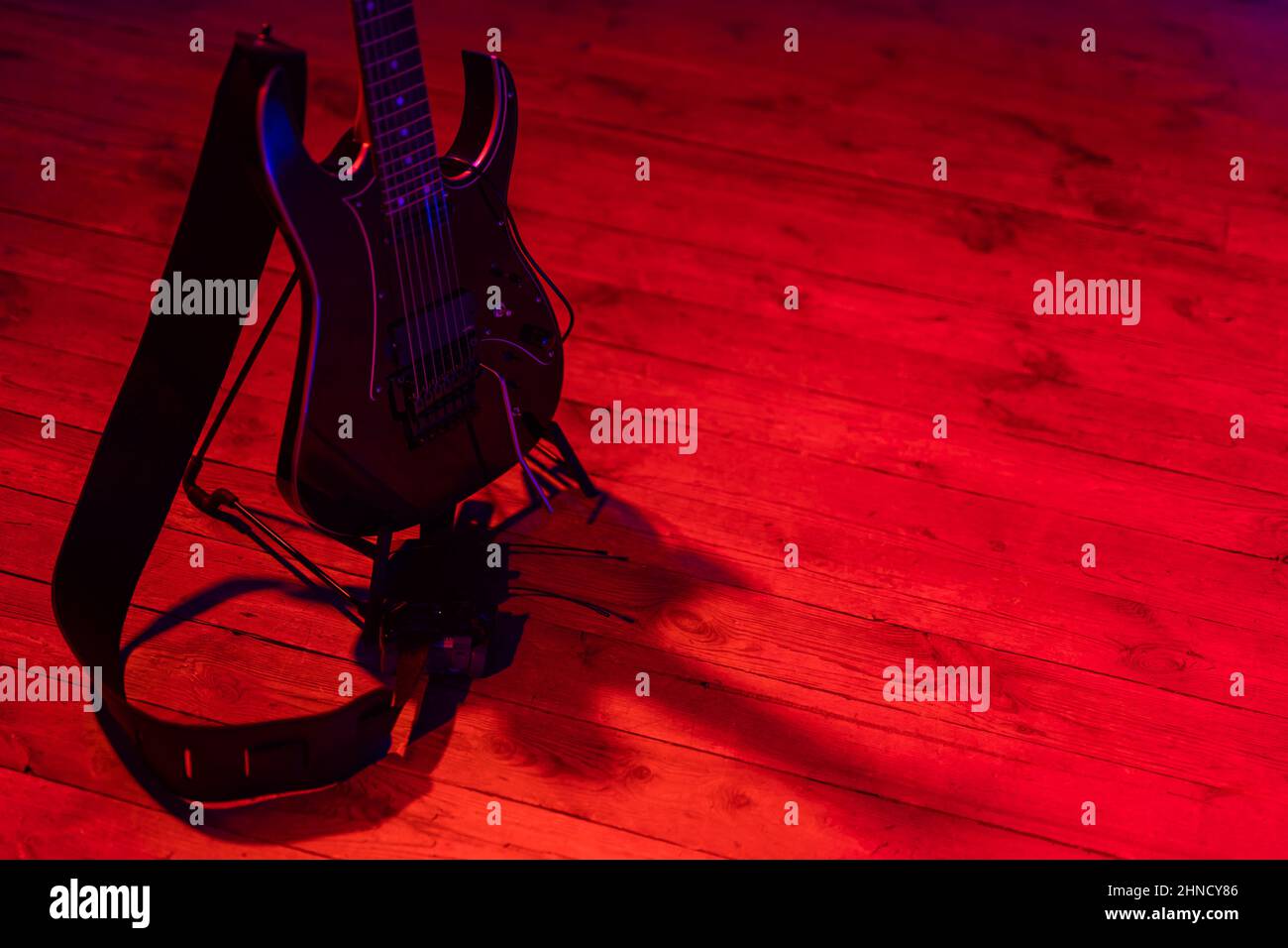 Eine schwarze E-Gitarre, die auf einem auf der Bühne platzierten Ständer basiert. Motiv wird durch starkes rotes Licht beleuchtet. Stockfoto