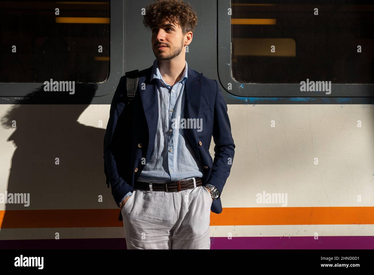 Schöner bärtiger hispanischer Mann, der wegschaut und in der Nähe des Zuges steht, während er am sonnigen Sommertag auf die Abfahrt auf dem Bahnsteig wartet Stockfoto
