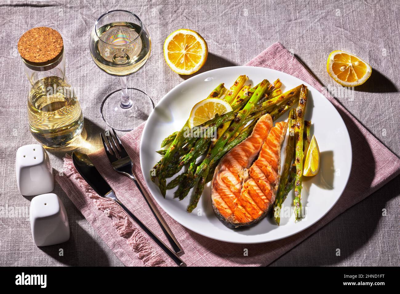 Gegrilltes Lachssteak mit gebratenem Spargel und Zitrone auf einem Teller auf einer Leinentischdecke Stockfoto