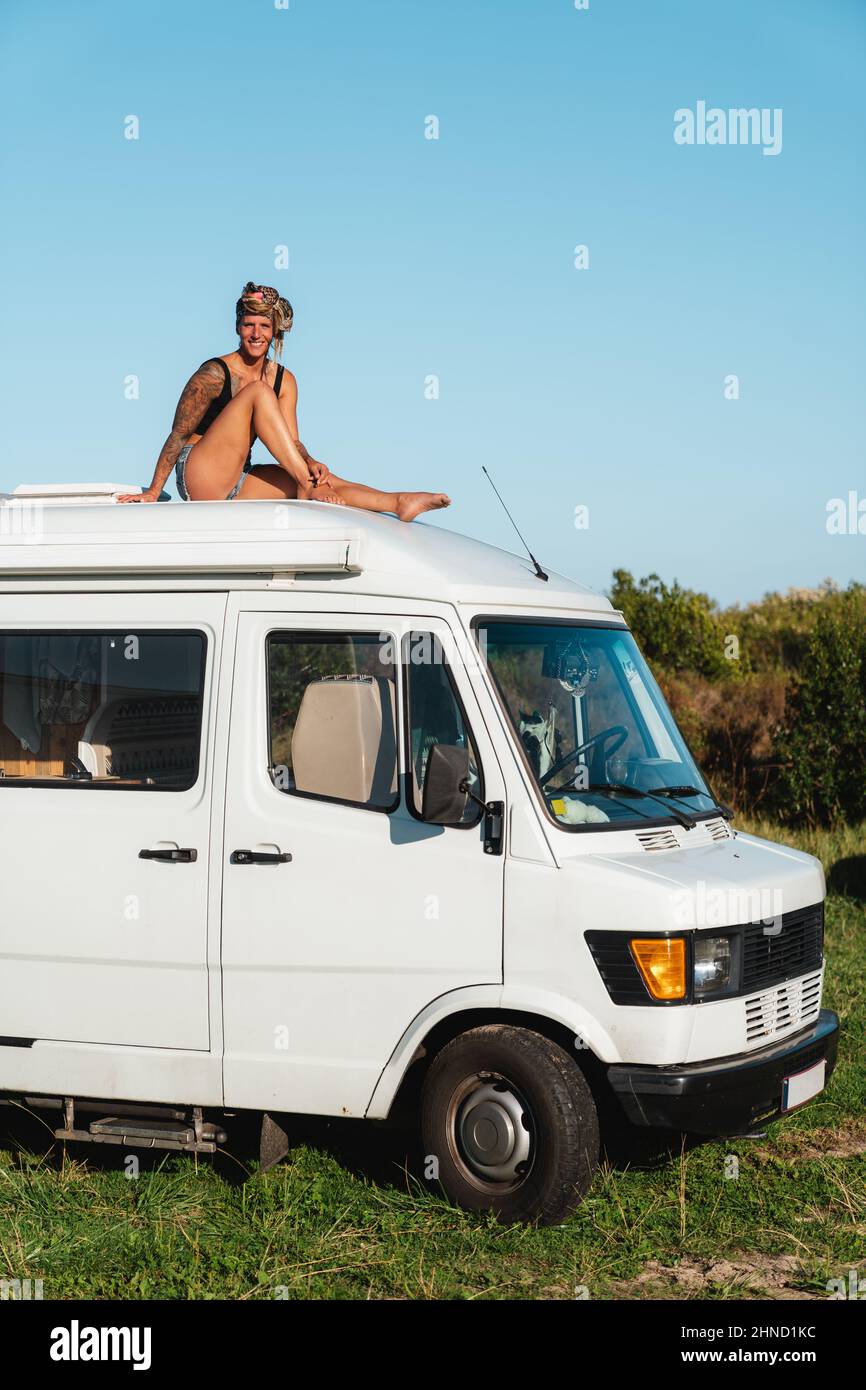 Voller Körper von angenehmen barfuß nachdenklichen Hippie weibliche Reisende sitzen auf dem Dach des weißen camping van in der Natur während der Reise geparkt Stockfoto