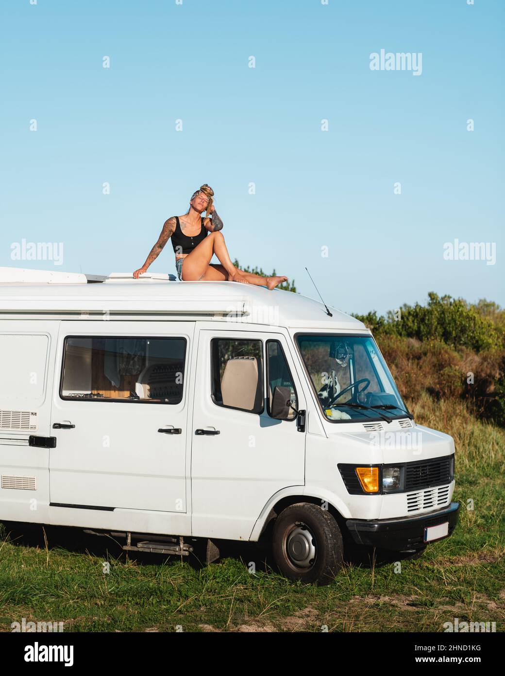 Voller Körper von angenehmen barfuß nachdenklich Hippie weibliche Reisende sitzen mit geschlossenen Augen auf dem Dach des weißen Camping van in der Natur während der Straße tr geparkt Stockfoto