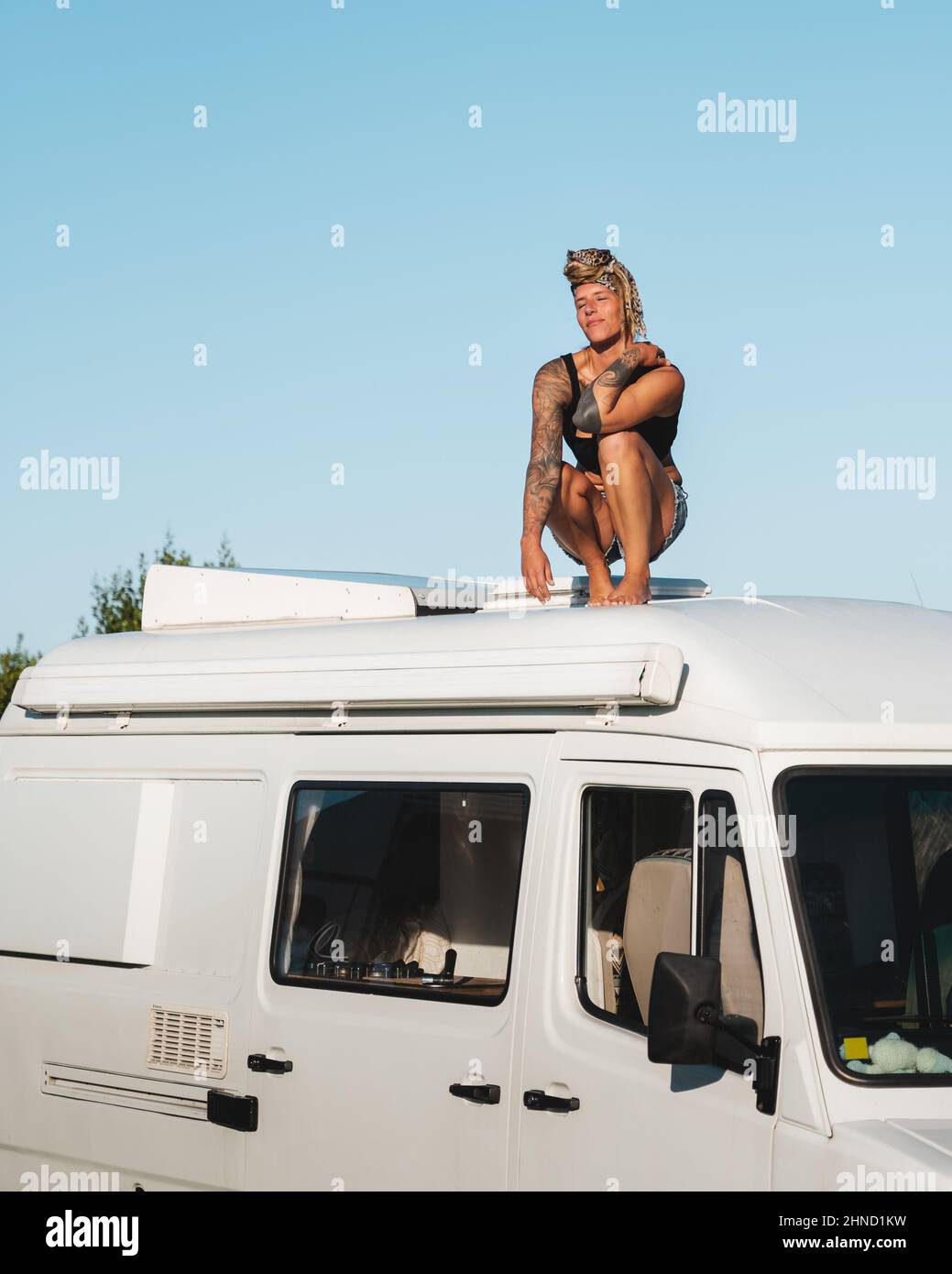 Voller Körper von angenehmen barfuß nachdenklich Hippie weibliche Reisende sitzen mit geschlossenen Augen auf dem Dach des weißen Camping van in der Natur während der Straße tr geparkt Stockfoto