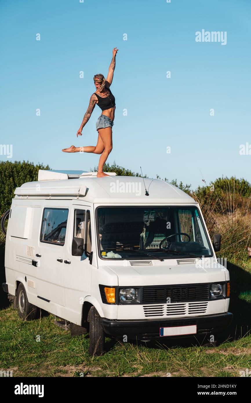 Voller Körper von angenehmen barfuß Hippie weibliche Reisende auf dem Dach des weißen Camping van in der Natur während der Fahrt geparkt stehen Stockfoto