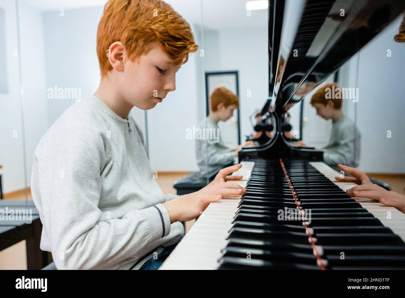 Seitenansicht des jungen Jungen, der Klavier spielt, während er im Klassenzimmer Melodie lernt Stockfoto