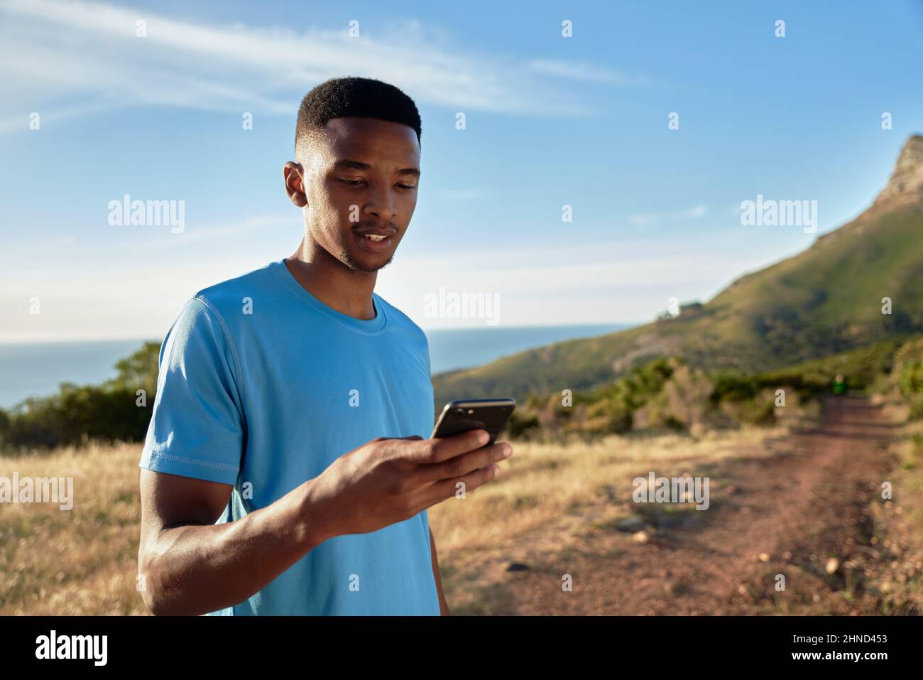 Schwarzer junger Erwachsener, der seinen Timer auf sein Telefon setzt, bevor er auf seinen Bergweglauf geht. Stockfoto