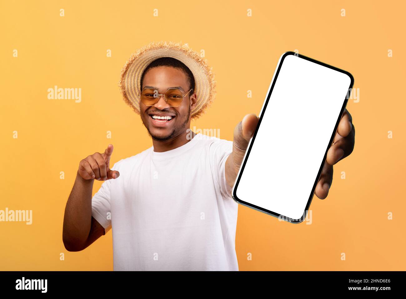 Aufgeregt schwarzer Mann im Sommer Hut zeigt Handy mit leerem Bildschirm, empfehlen mobile App für Reisen Stockfoto