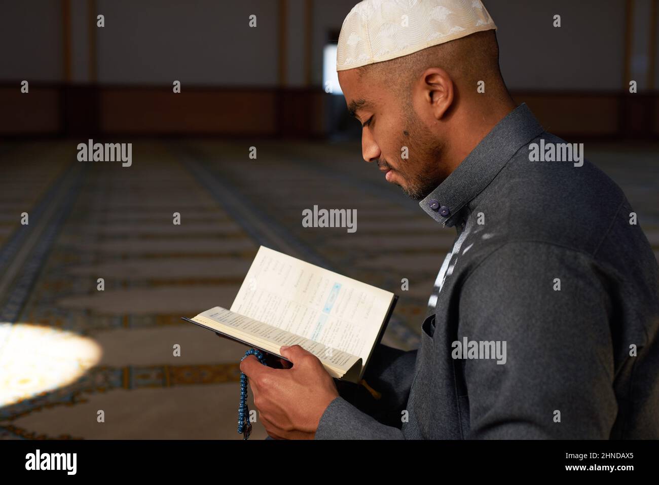 Seitenansicht eines jungen muslimischen Mannes, der lächelte und den Koran las Stockfoto