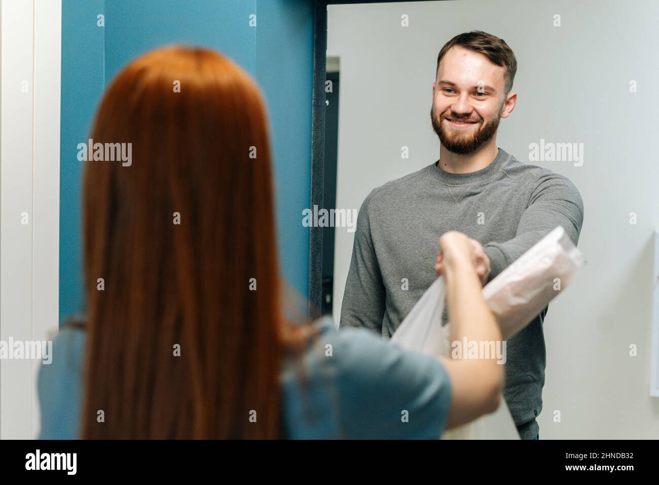 Fröhlicher bärtiger Kurier männlich liefert Lebensmittelbeutel mit zu unkenntlich weiblichen Hausfrau Kunde auf Tür zu Hause. Stockfoto