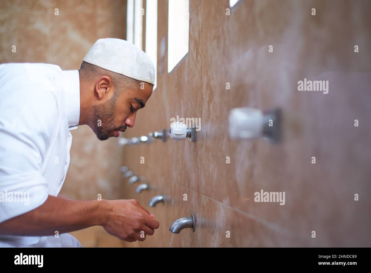 Ein muslimischer Mann, der sein Gesicht im Waschraum mit Wasser reinigt Stockfoto