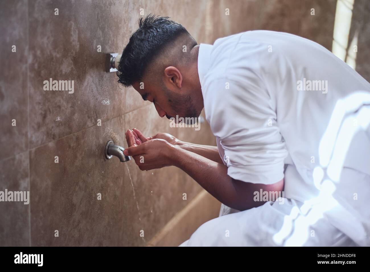 Ein junger Muslim, der sein Gesicht im Waschraum mit Wasser reinigt Stockfoto