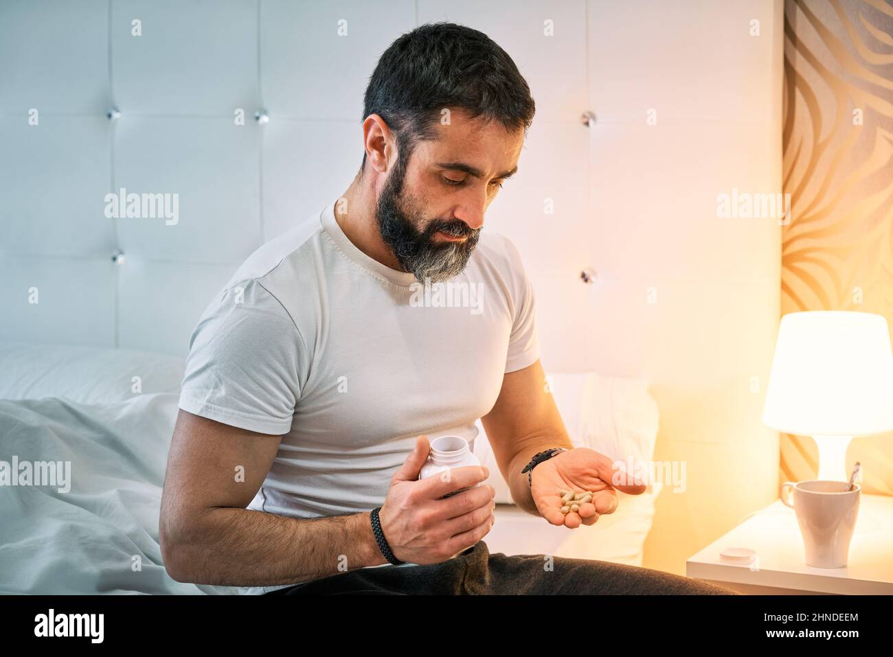 Person mit einem Problem auf dem Bett sitzen und auf der Suche nach einer Pille Stockfoto