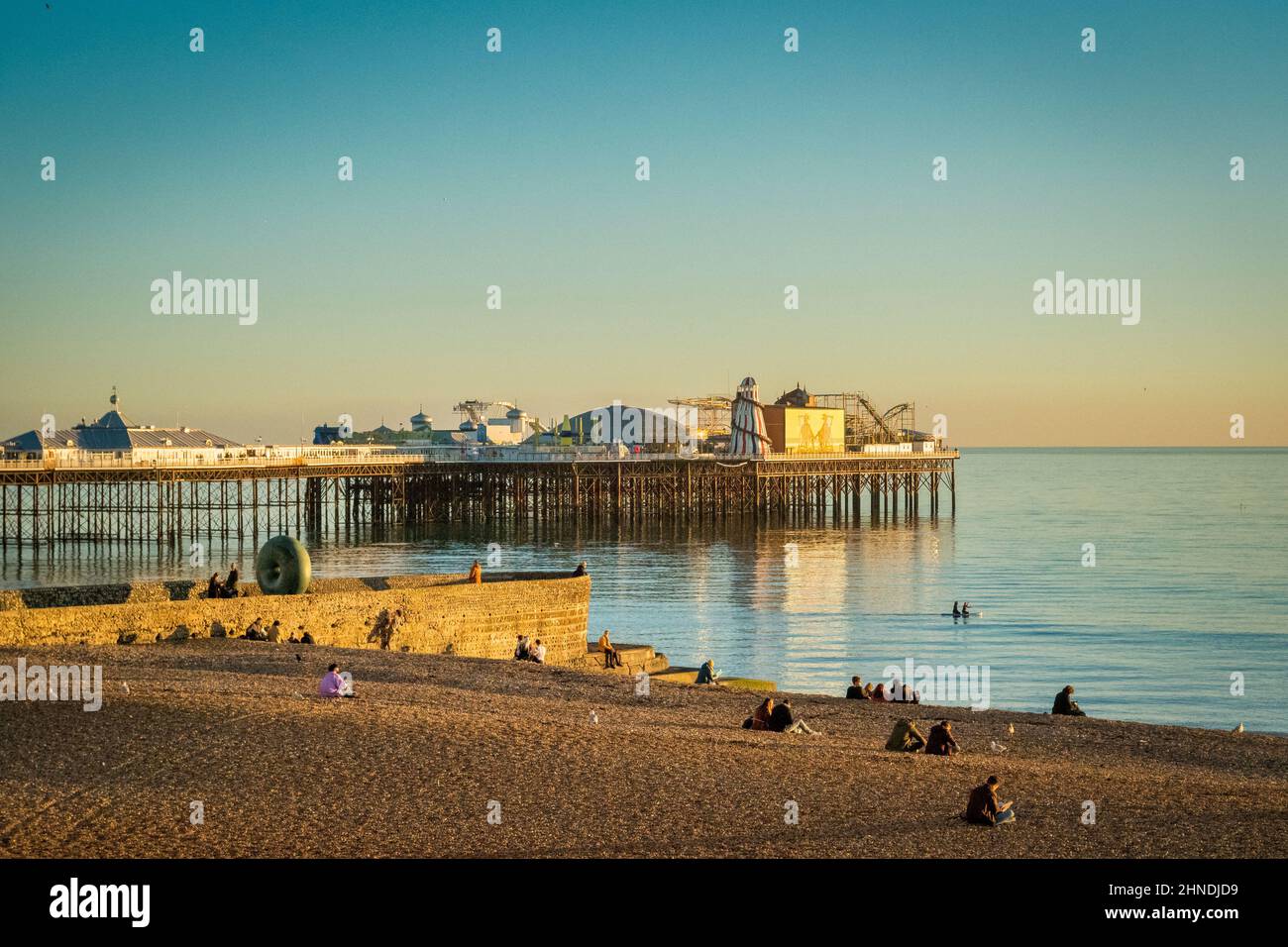 13. Januar 2022: Brighton, East Sussex, Großbritannien - Menschen, die an einem klaren Winterabend am Brighton Beach bei Sonnenuntergang sitzen, in der Nähe der Doughnut Groyne und... Stockfoto