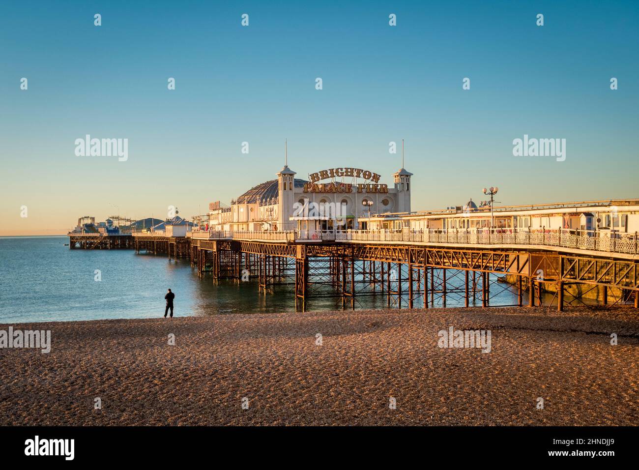 14. Januar 2022: Brighton, East Sussex, Großbritannien - Sonnenaufgang am Brighton Palace Pier, mit einem Mann, der am Strand steht und aufs Meer blickt. Stockfoto